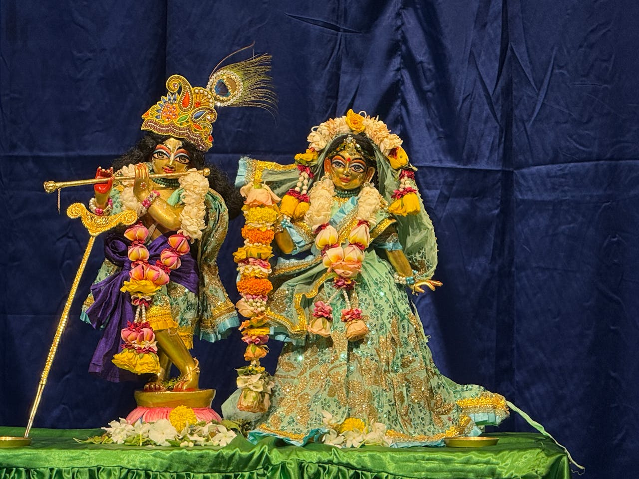 Home Colorful statues of Hindu deities adorned with vibrant floral garlands, set against a blue backdrop.