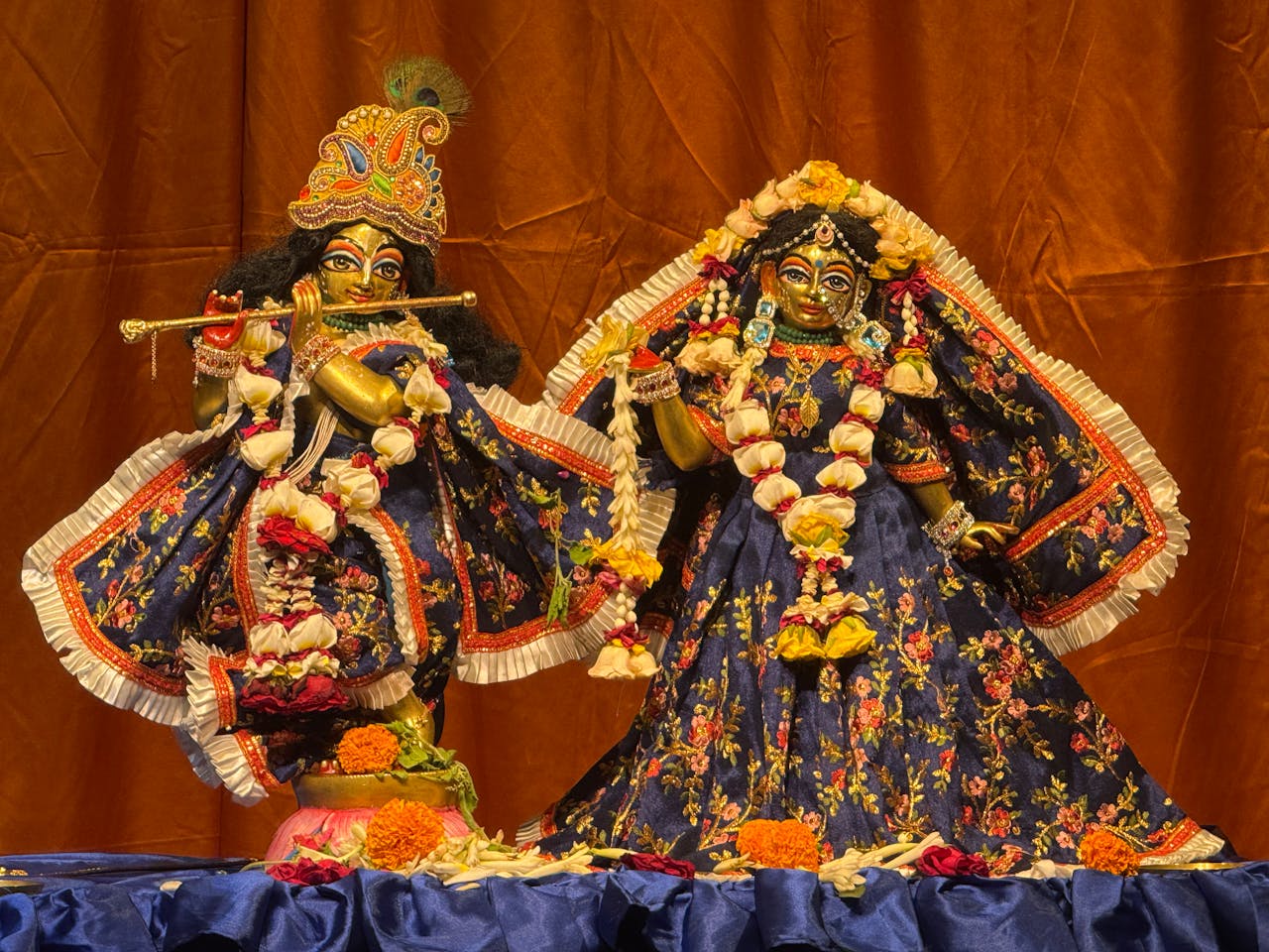 Home Elegant Hindu deity statues adorned with floral garlands and detailed attire on display.